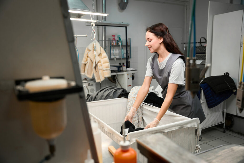 Smiling woman dry-cleaning operator sorting clothes, checking on presence of stains and tears before cleaning in washing mashine